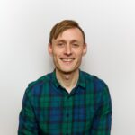 Chris Sampson - OHE Smiling man in a green and blue plaid shirt against a light plain background.