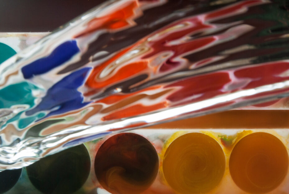 Close-up of a painter's palette with circular paint wells in browns and yellows and swirling colorful patterns above.