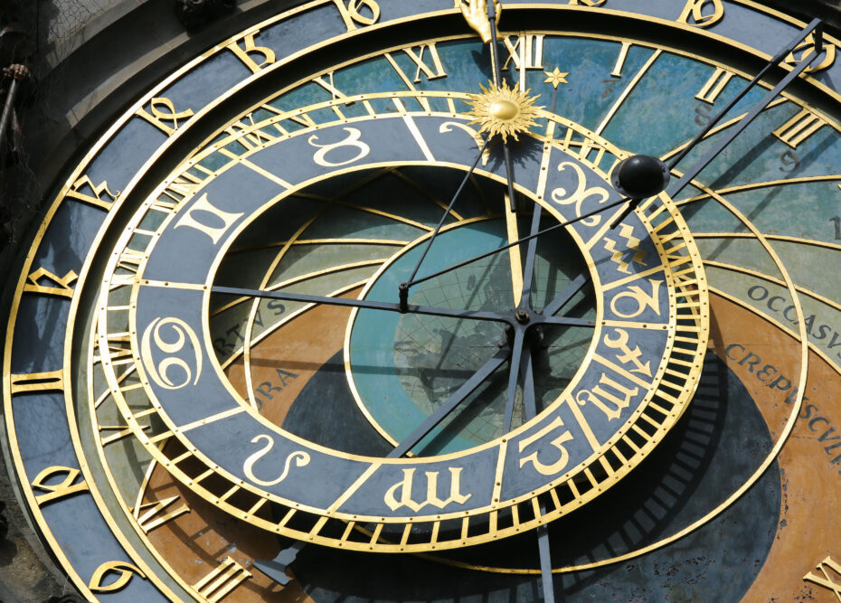 Close-up of a historic astronomical clock with gold Roman numerals and a sun emblem on a multi-colored dial.