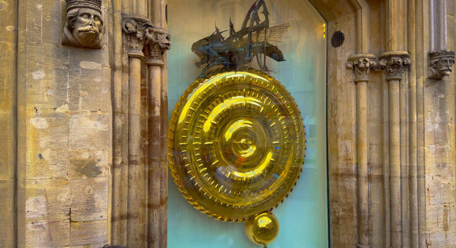 Ornate stone storefront with a large gold circular ornament in a window display; a dragon figure looms above the circle.