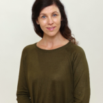 Priscila Radu - OHE Portrait of a woman with blue eyes and dark brown hair, wearing an olive green sweater, facing slightly to the left with a soft smile.