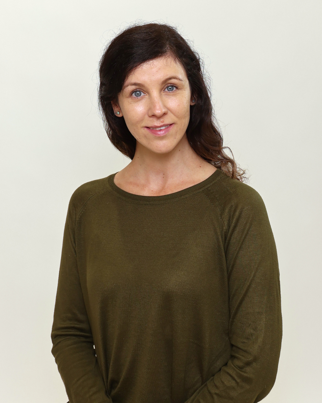 Portrait of a woman with blue eyes and dark brown hair, wearing an olive green sweater, facing slightly to the left with a soft smile.