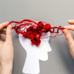 A human head paper cut out with tangled red yarn above symbolising the brain