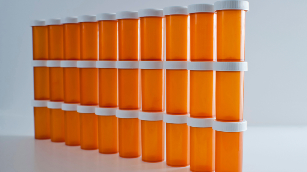 Three rows of identical orange prescription bottles with white lids and labels, arranged neatly in a line, increasing in height from left to right against a white background.