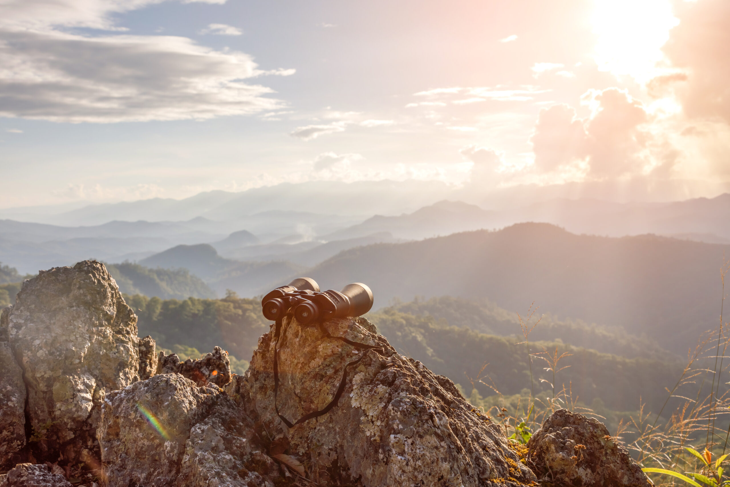 binoculars on top of rock mountain at beautiful sunset background