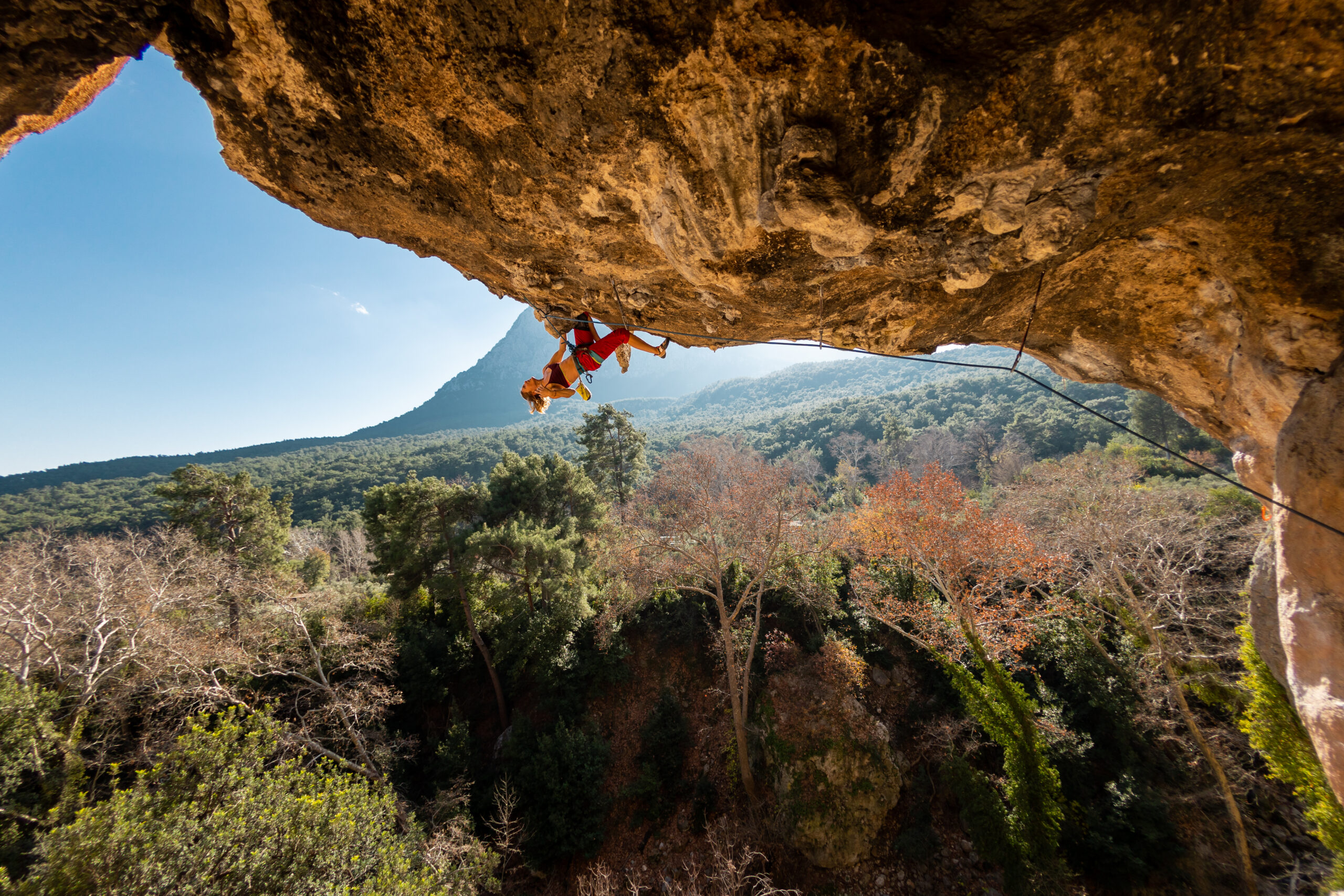Girl climber on an overhanging rock A sports woman climbs a rock against the backdrop of mountains difficult movements in rock climbing