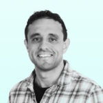 Tim Reason - OHE Smiling man in a plaid shirt facing the camera against a light teal background (head and shoulders).