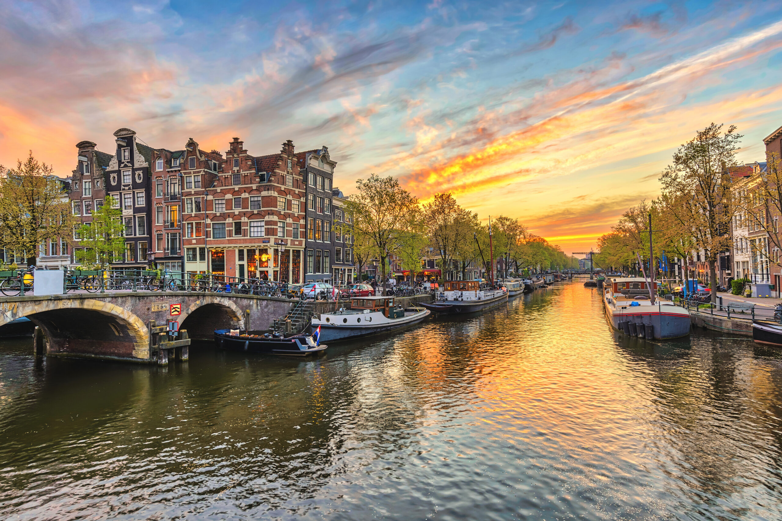 Sunset over a canal with historic brick buildings on the left and boats docked along the waterway