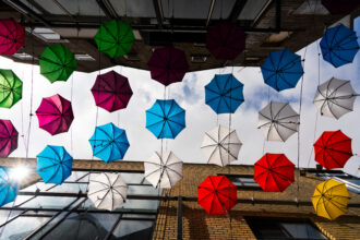 the colored umbrellas on the sky in Dublin Ireland - OHE Colorful umbrellas suspended overhead between brick buildings, creating a vibrant canopy above the street.