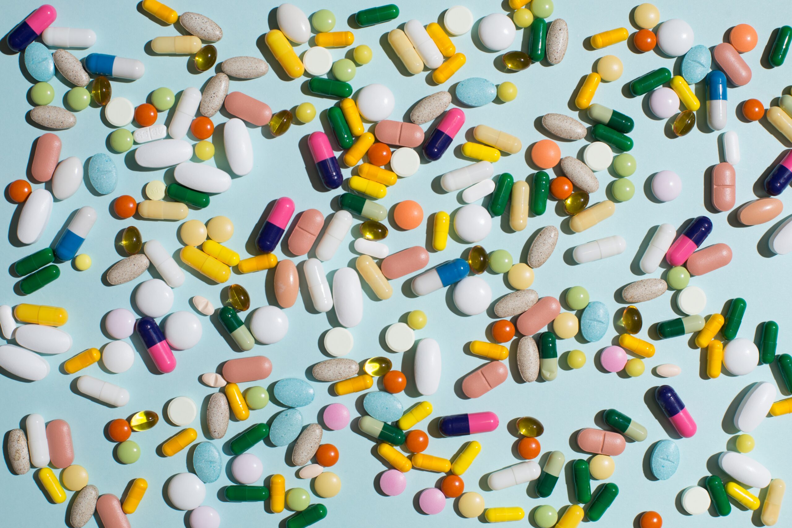 Assorted colorful pills and capsules scattered across a light blue surface.