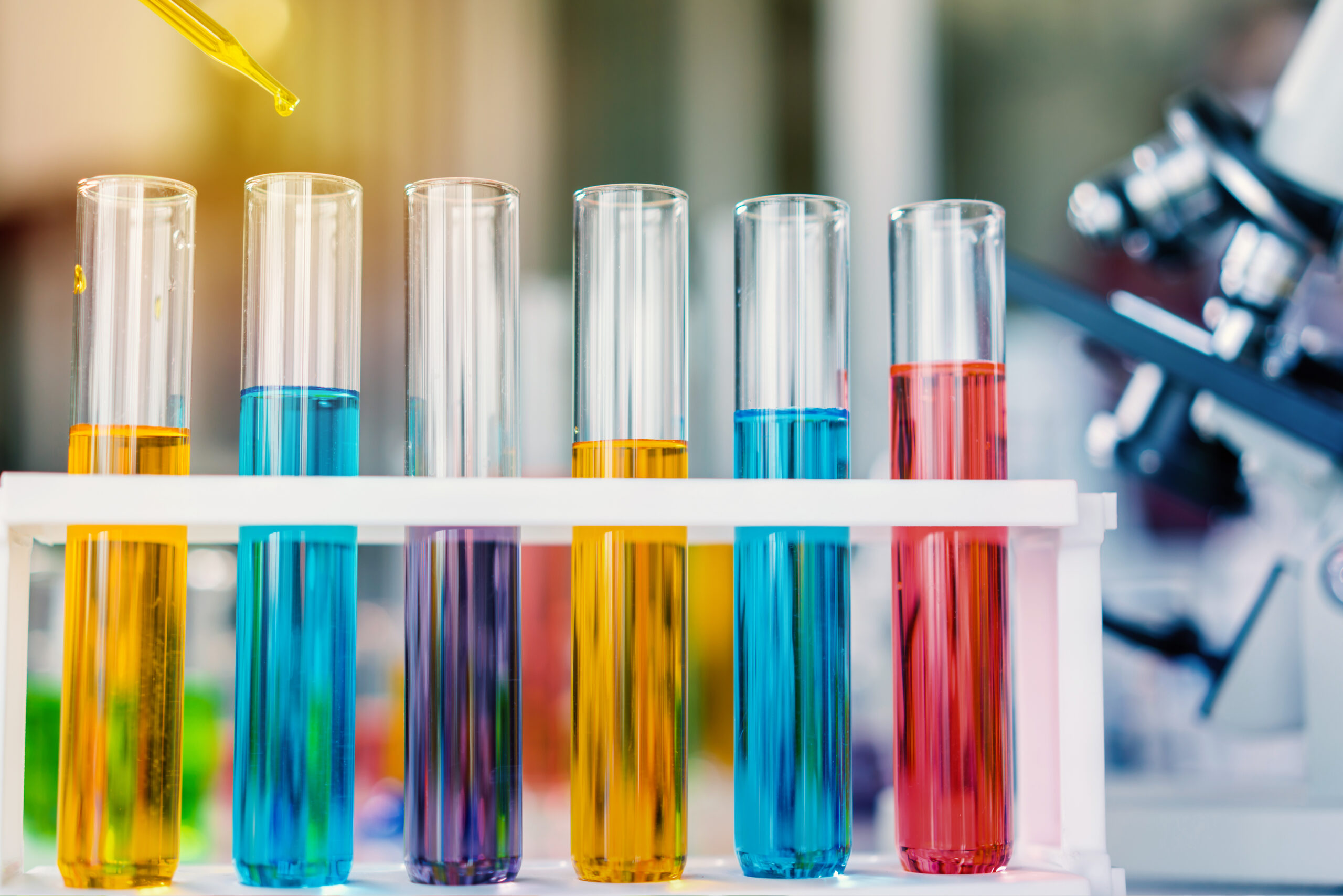 Row of clear test tubes in a rack containing vibrant colored liquids in a laboratory setting