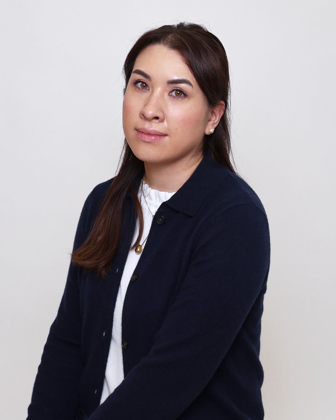 Portrait of a woman with long dark hair, wearing a navy cardigan over a white blouse, against a neutral background.