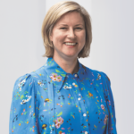 Dr Samantha Roberts - OHE Smiling woman with short blonde hair wearing a blue floral blouse, standing against a light background.