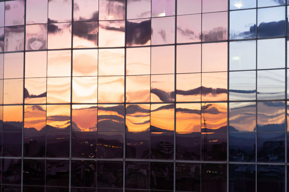 sunset reflection in windows of modern building with windows and orange and pink colored windows texture background - OHE Glass facade reflecting a colorful sunset with pink, orange, and blue skies.