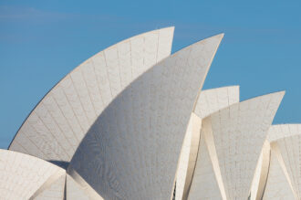 White sail-shaped roofs of the Sydney Opera House against a clear blue sky.